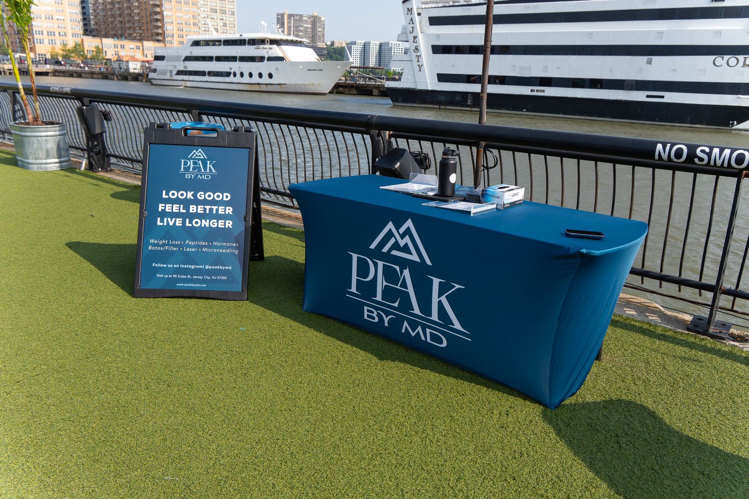 Peak by MD branded table setup outdoors at a waterfront event with a motivational sign promoting health and wellness.