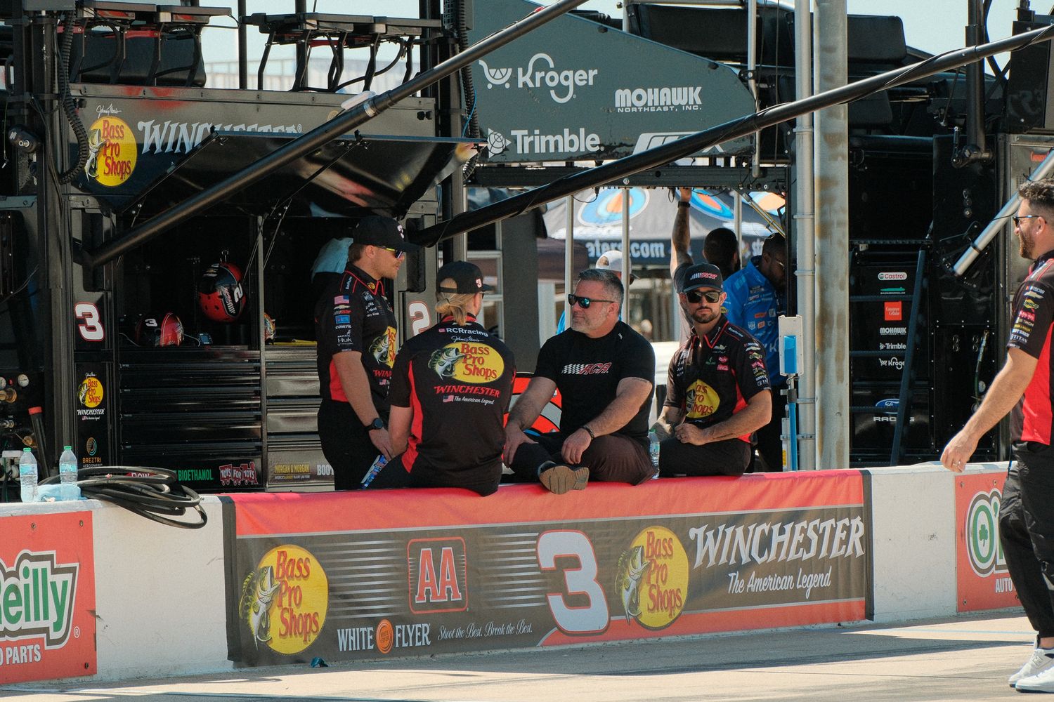 NASCAR Bass Pro Shops No. 3 pit crew members gather near the garage wall at a Kroger-sponsored race event.
