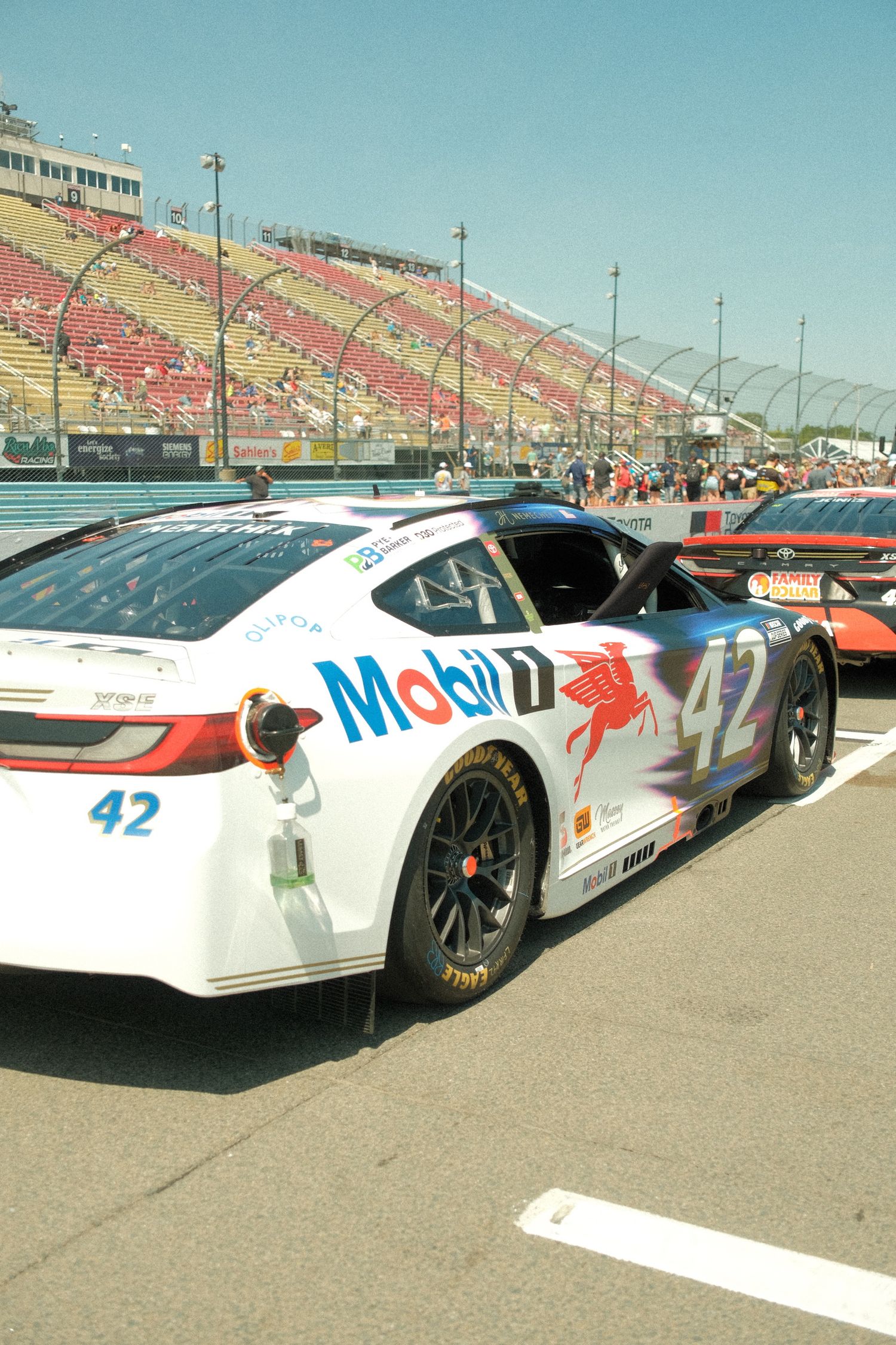 NASCAR number 42 Mobil 1 sponsored white race car parked on pit road at a sunny speedway.