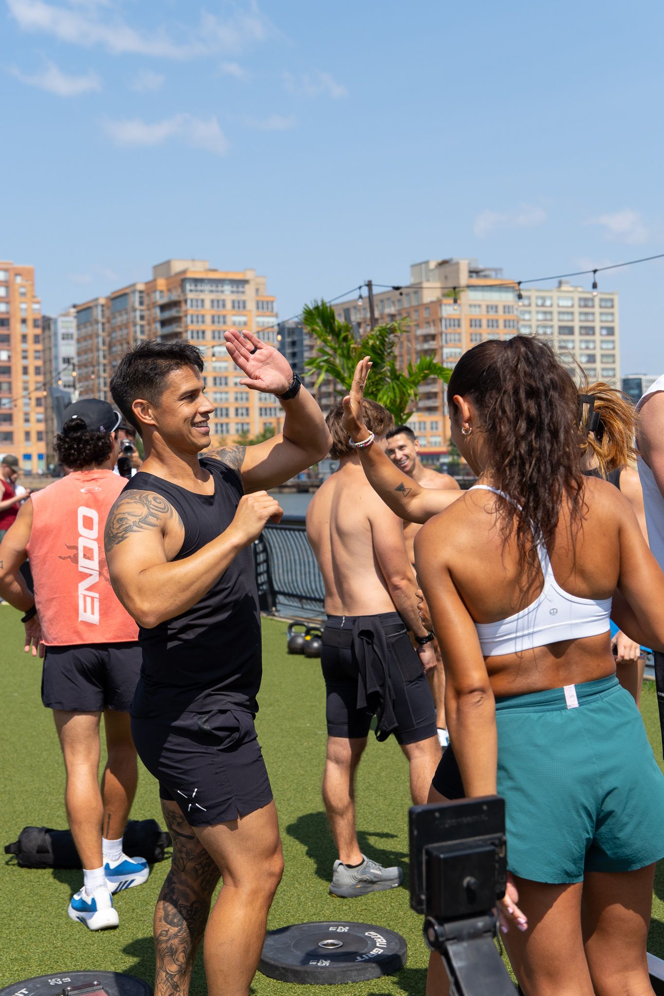 Two athletes high-fiving outdoors during a group fitness workout event on a sunny day.
