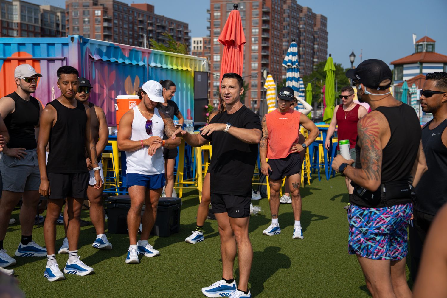 Group of athletes in athletic wear gathered on turf listening to an instructor at an outdoor fitness event.