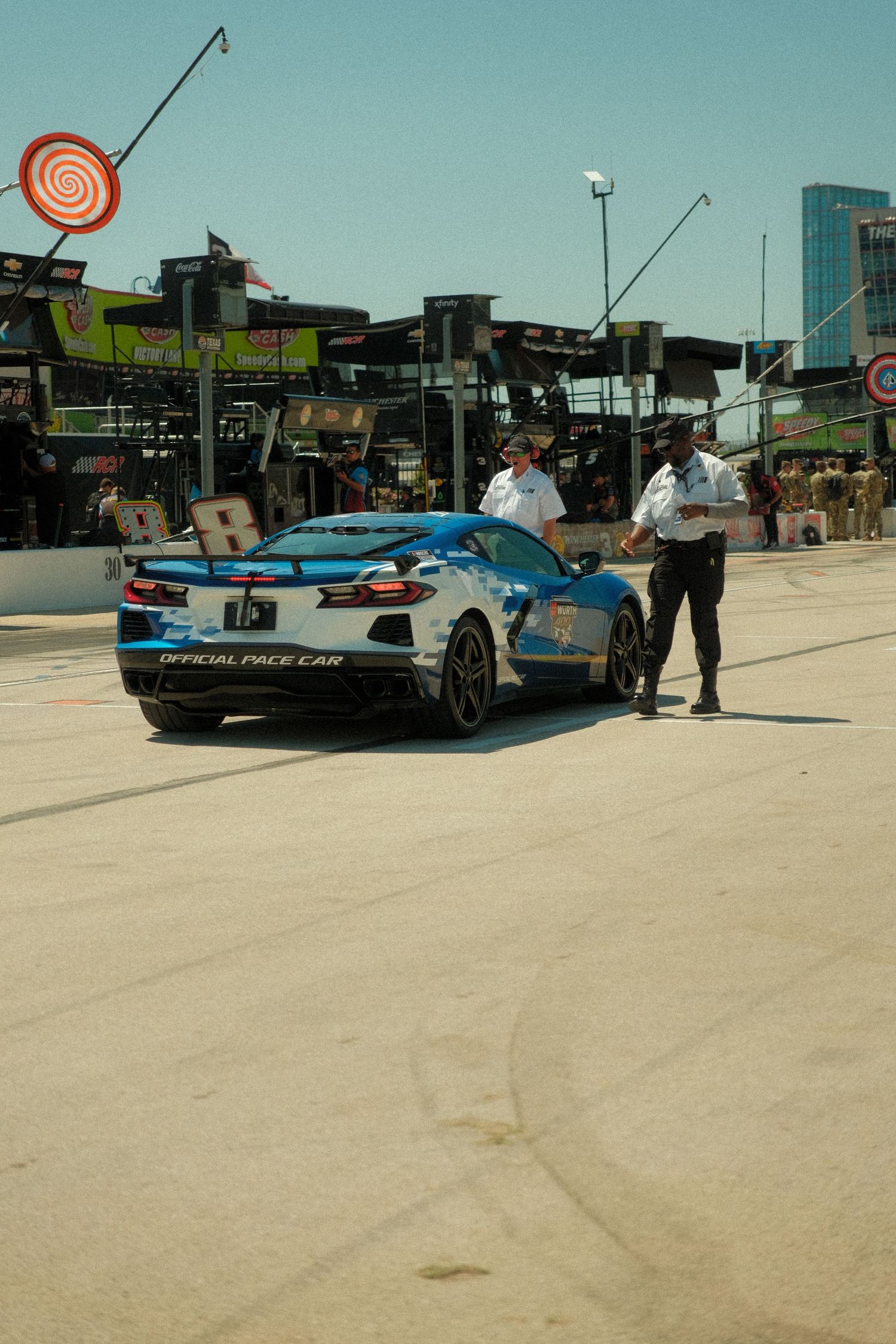 Official pace car Corvette parked in pit lane with two officials reviewing documents at a racing event.