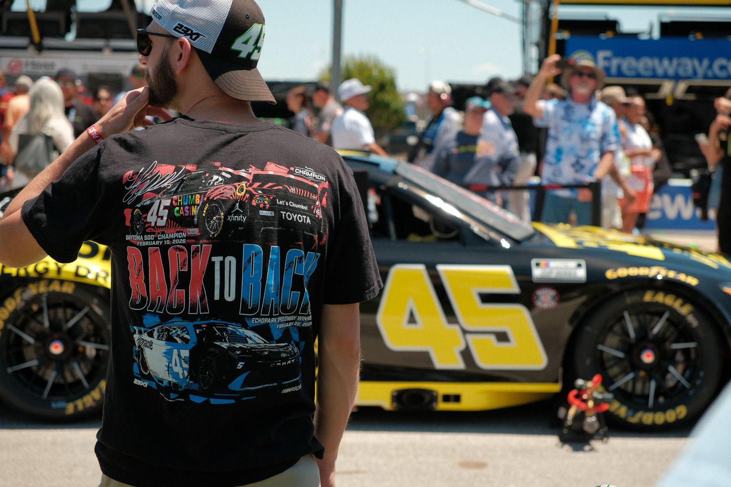 NASCAR fan wearing Back to Back shirt stands near No. 45 race car at Freeway speedway.