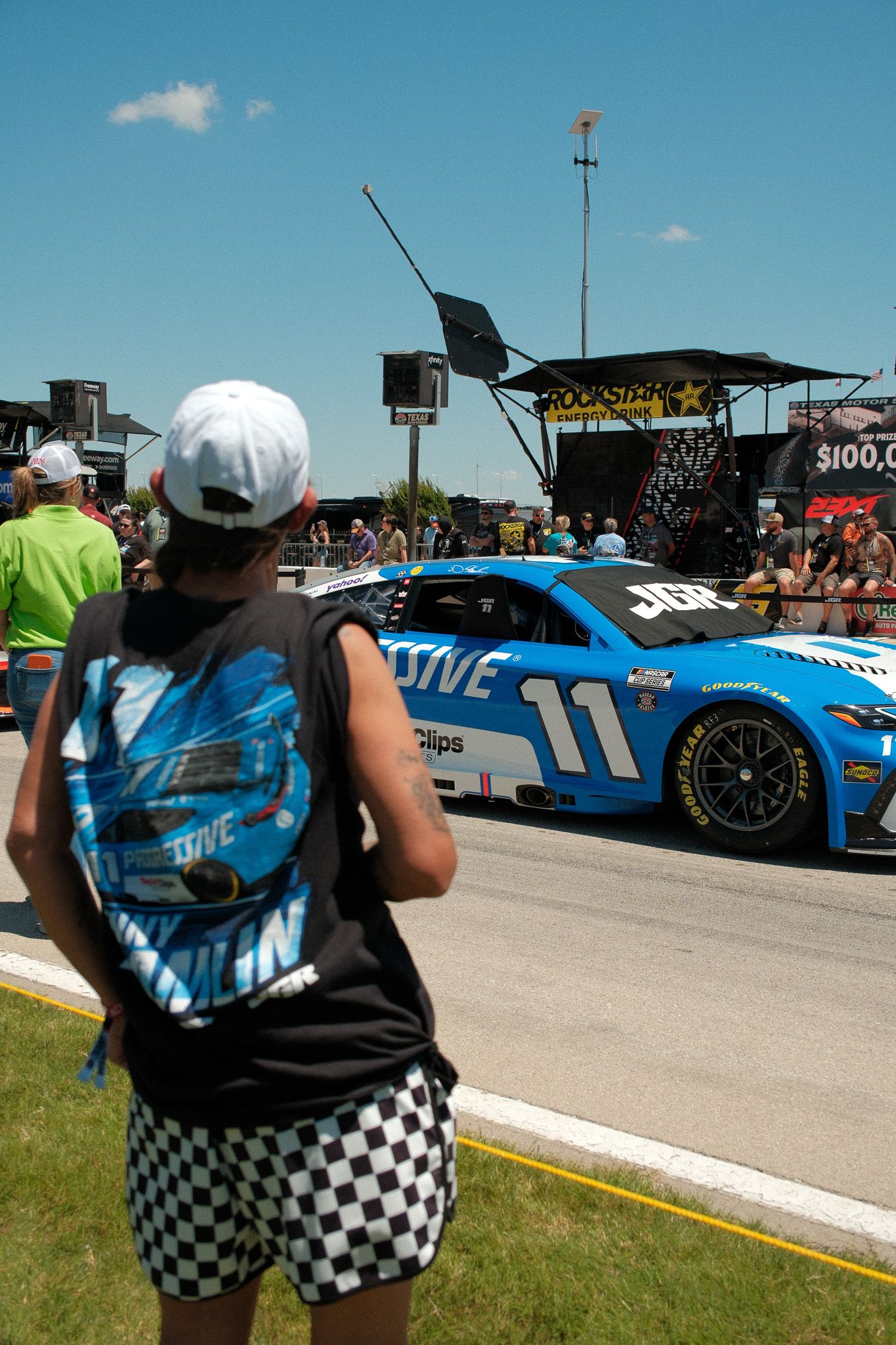NASCAR fan photographs the No. 11 Joe Gibbs Racing Toyota during a sunny race day event at the track.