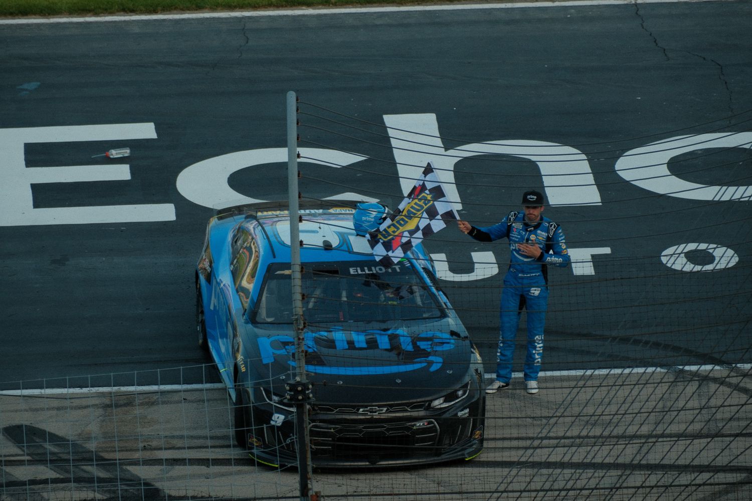 NASCAR race car driver celebrates victory with checkered flag at Echo speedway finish line.