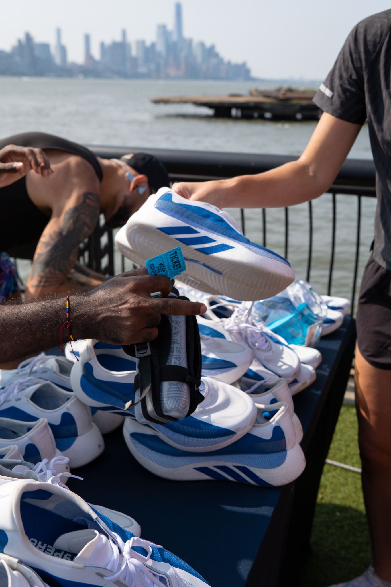 Adidas blue and white sneakers displayed on a table outdoors with NYC skyline in background.
