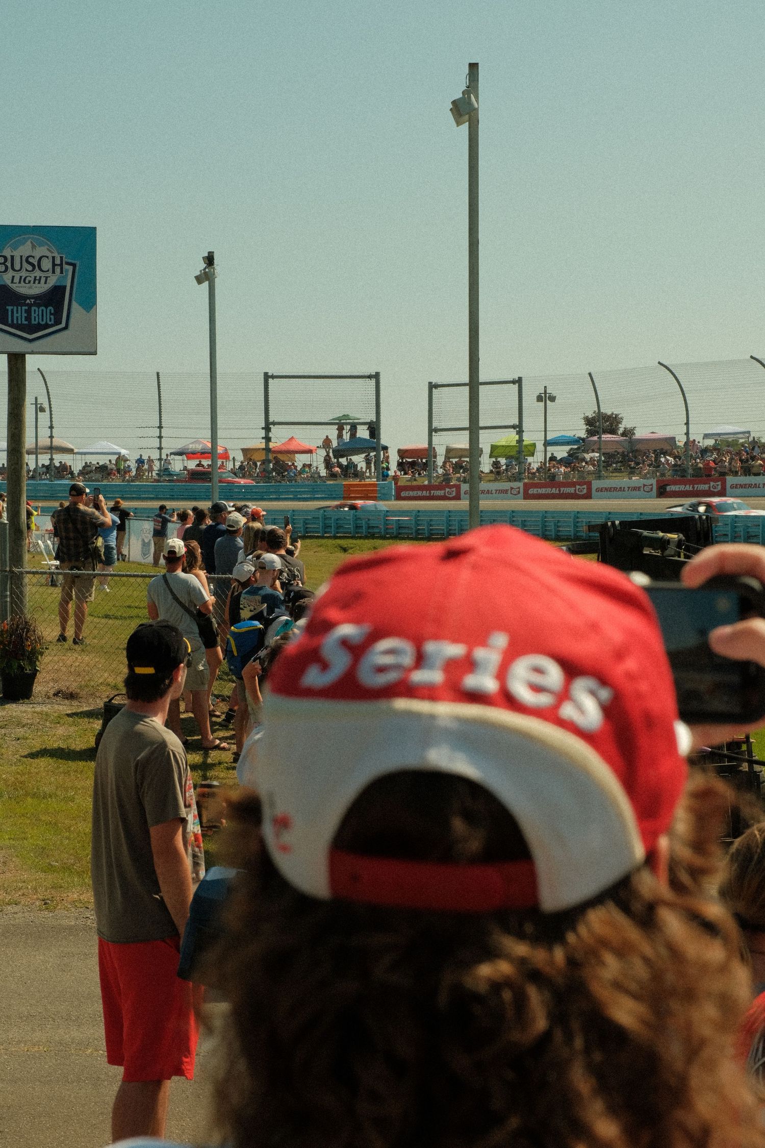 NASCAR fan wearing red Series cap watching race action at Busch Light sponsored track.