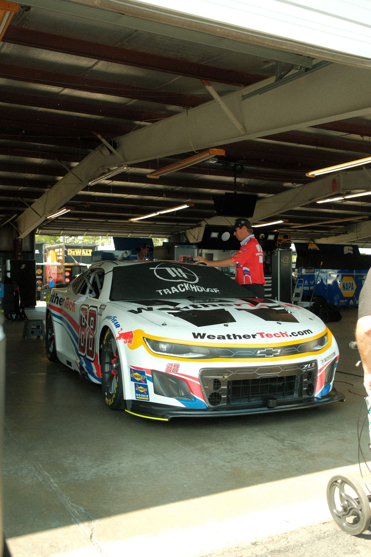 WeatherTech.com sponsored NASCAR Chevrolet Camaro ZL1 race car parked inside garage stall at racing event.