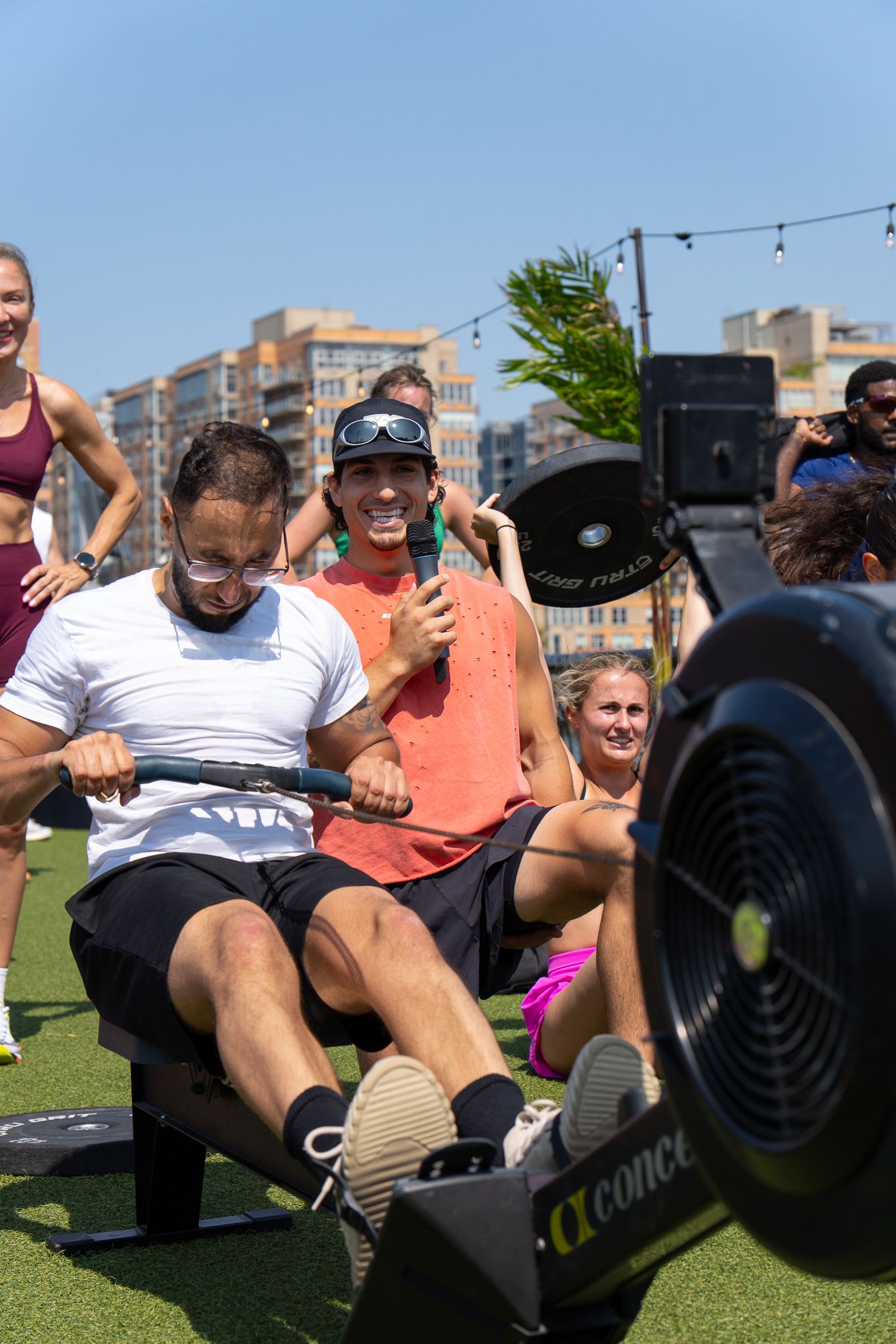 Group of athletes using a Concept2 rowing machine outdoors during a fitness event on a sunny day.