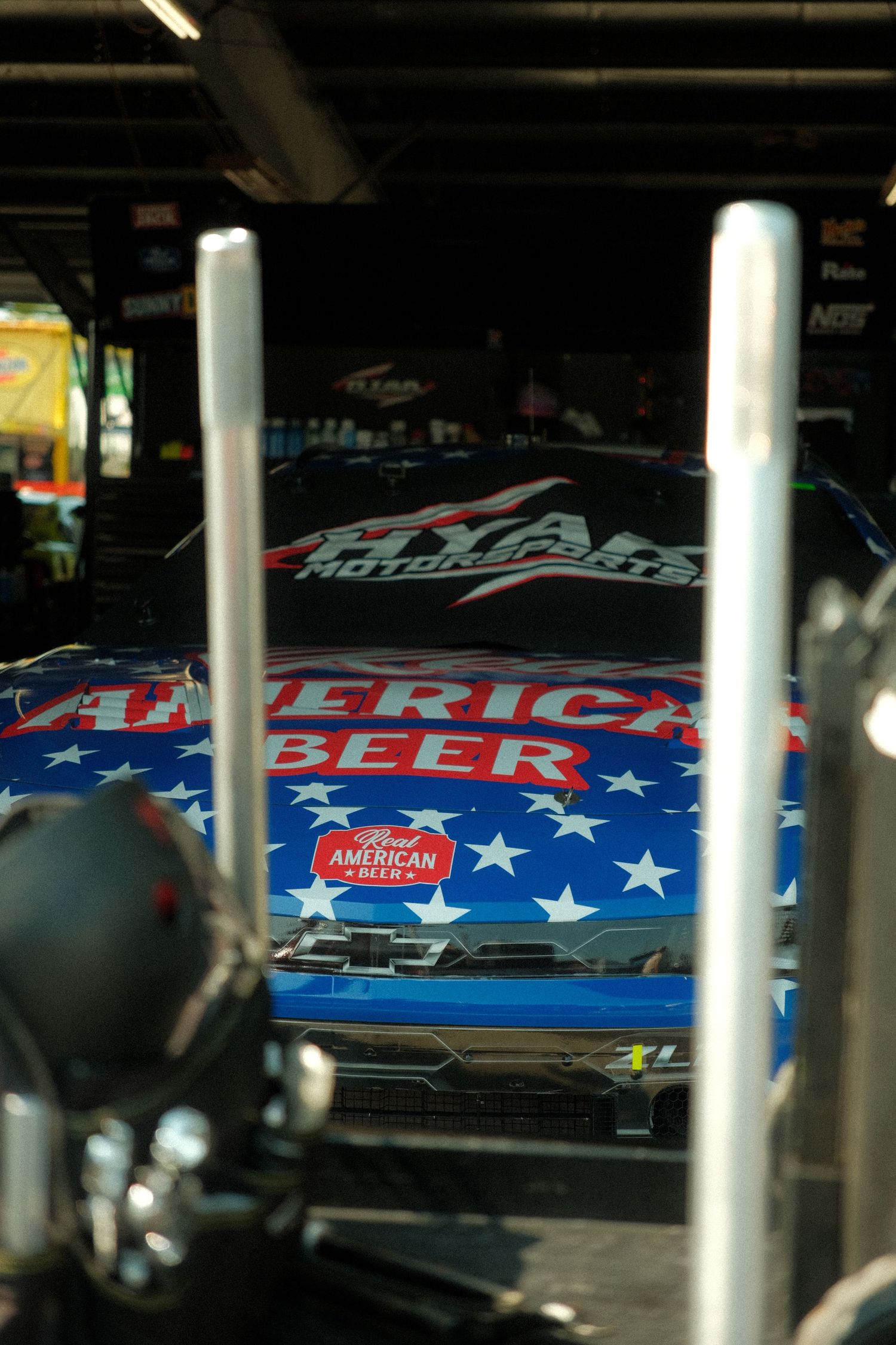 American Beer sponsored NASCAR Chevrolet race car with patriotic stars and stripes livery in dark garage.