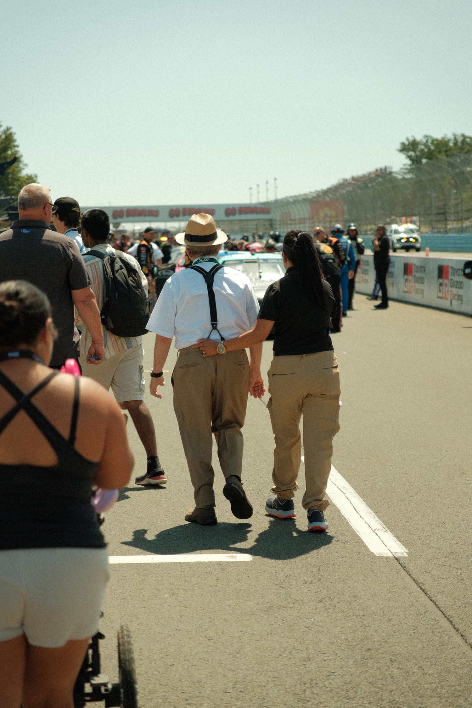 Crowd of spectators walking along the pit road at a NASCAR race event on a hot sunny day.