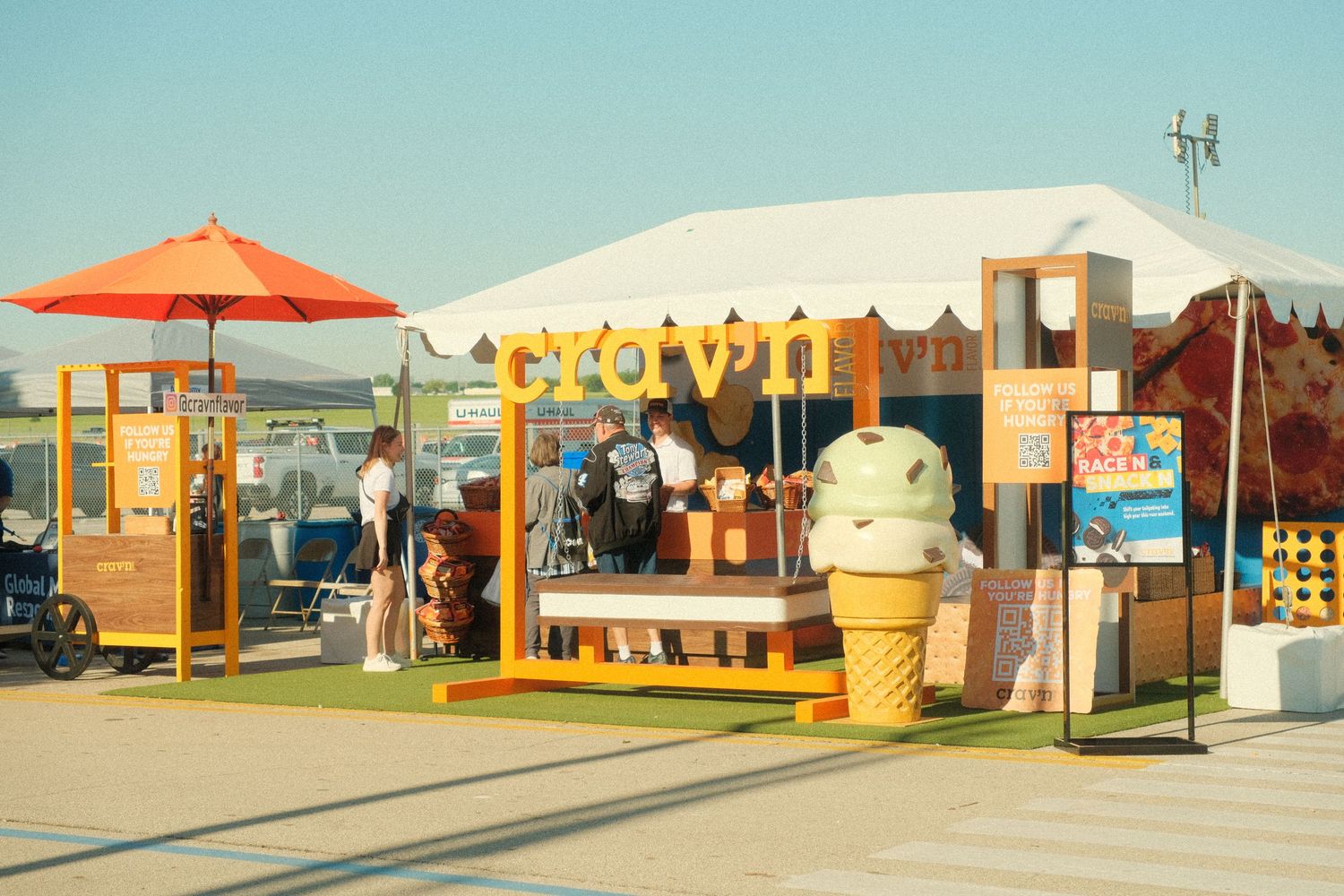 Crown ice cream booth with giant cone statue, orange umbrella, and wooden signage at an outdoor event.