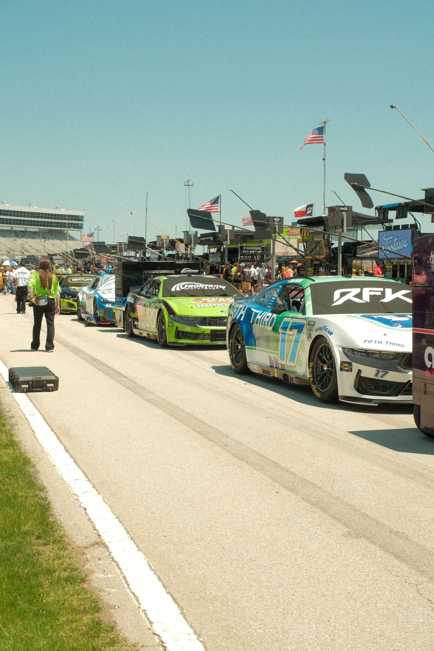 NASCAR race cars lined up in pit lane at a sunny speedway with RFK Racing car visible.