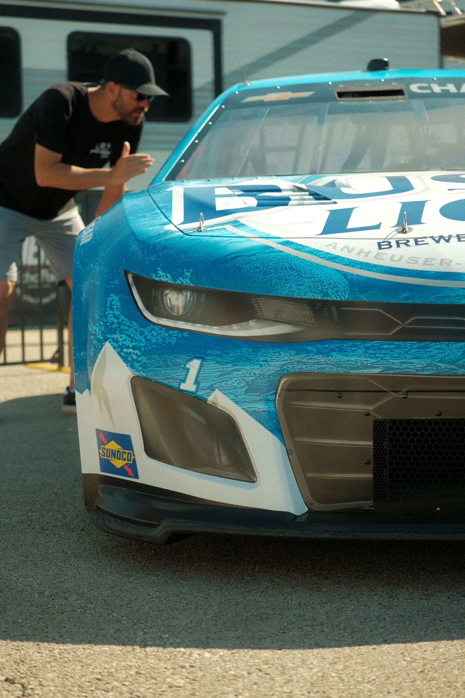 A NASCAR crew member inspects the blue Bud Light sponsored Chevrolet race car number 1 in the pit area.