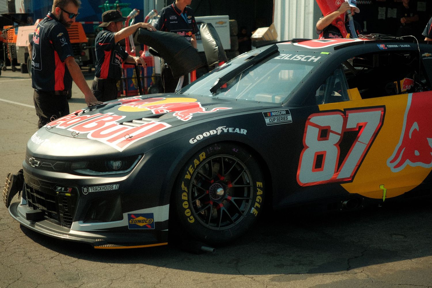 NASCAR number 87 Red Bull and Busch sponsored dark race car in the garage area at a speedway.