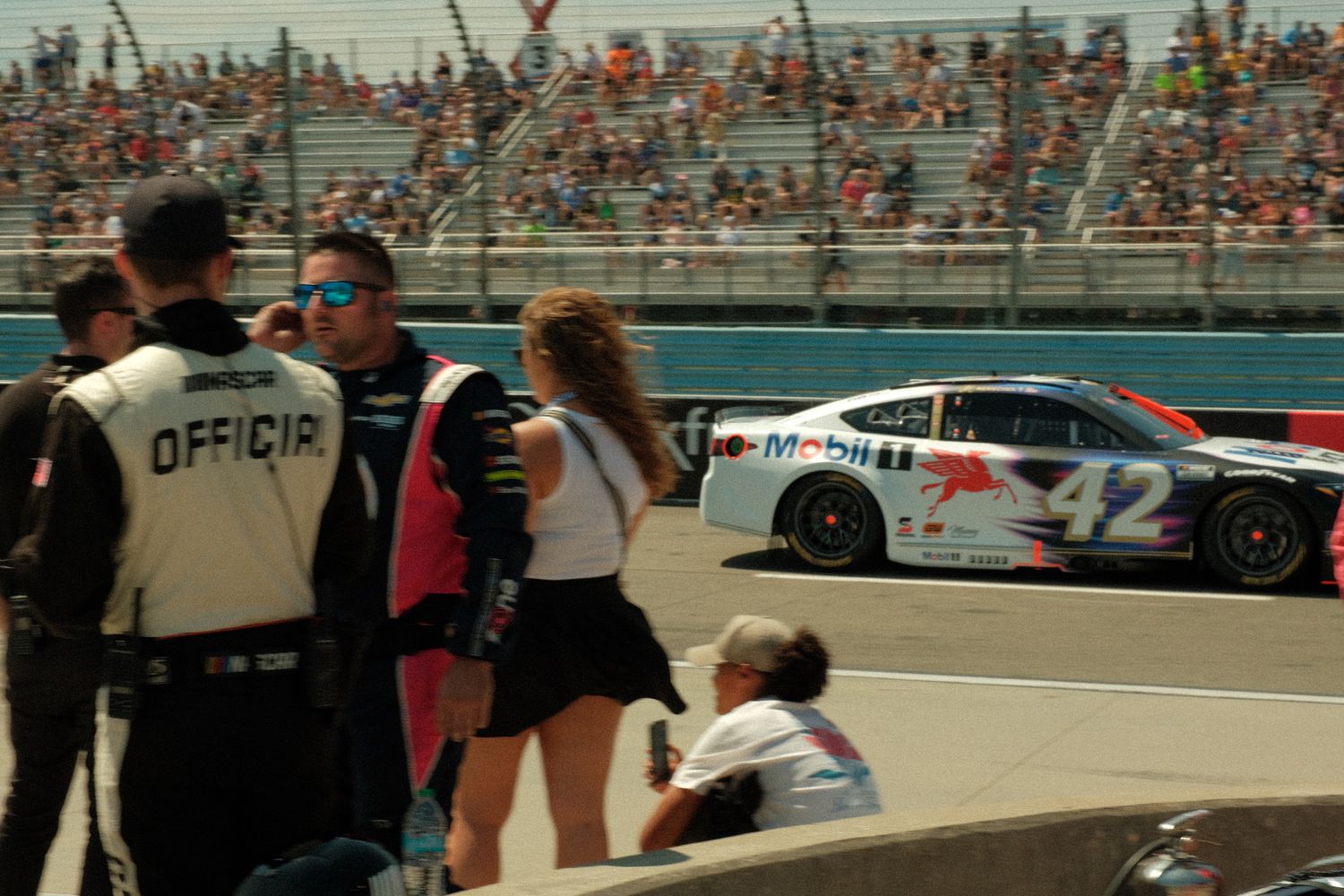 NASCAR official and spectators watch car number 12 with Mobil 1 sponsorship race past packed grandstands.