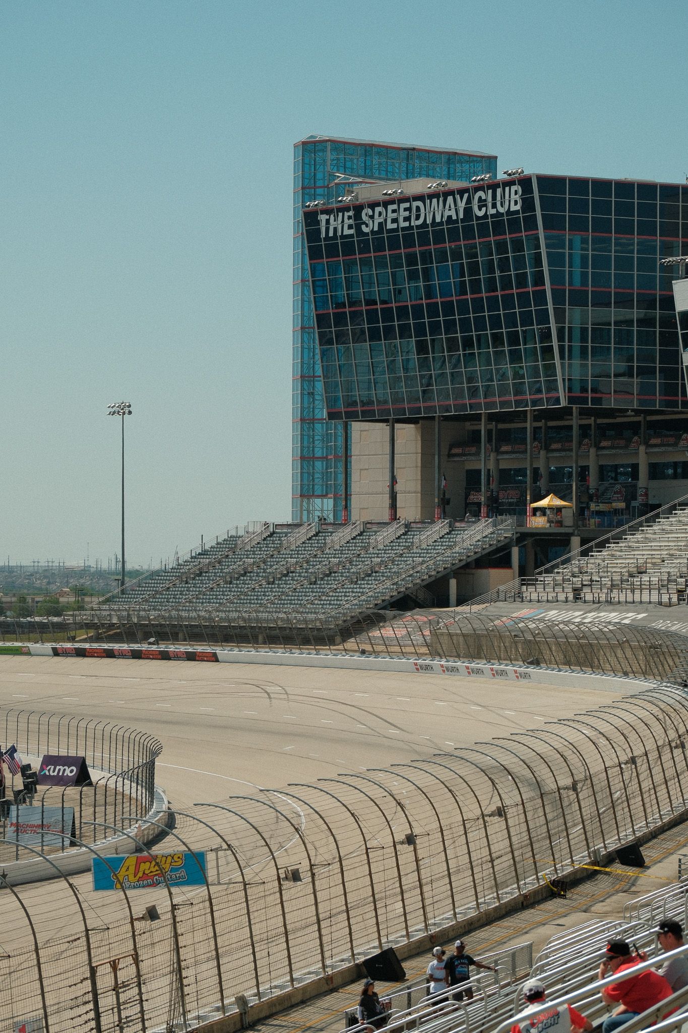 The Speedway Club building overlooks empty grandstands and race track on a clear day.