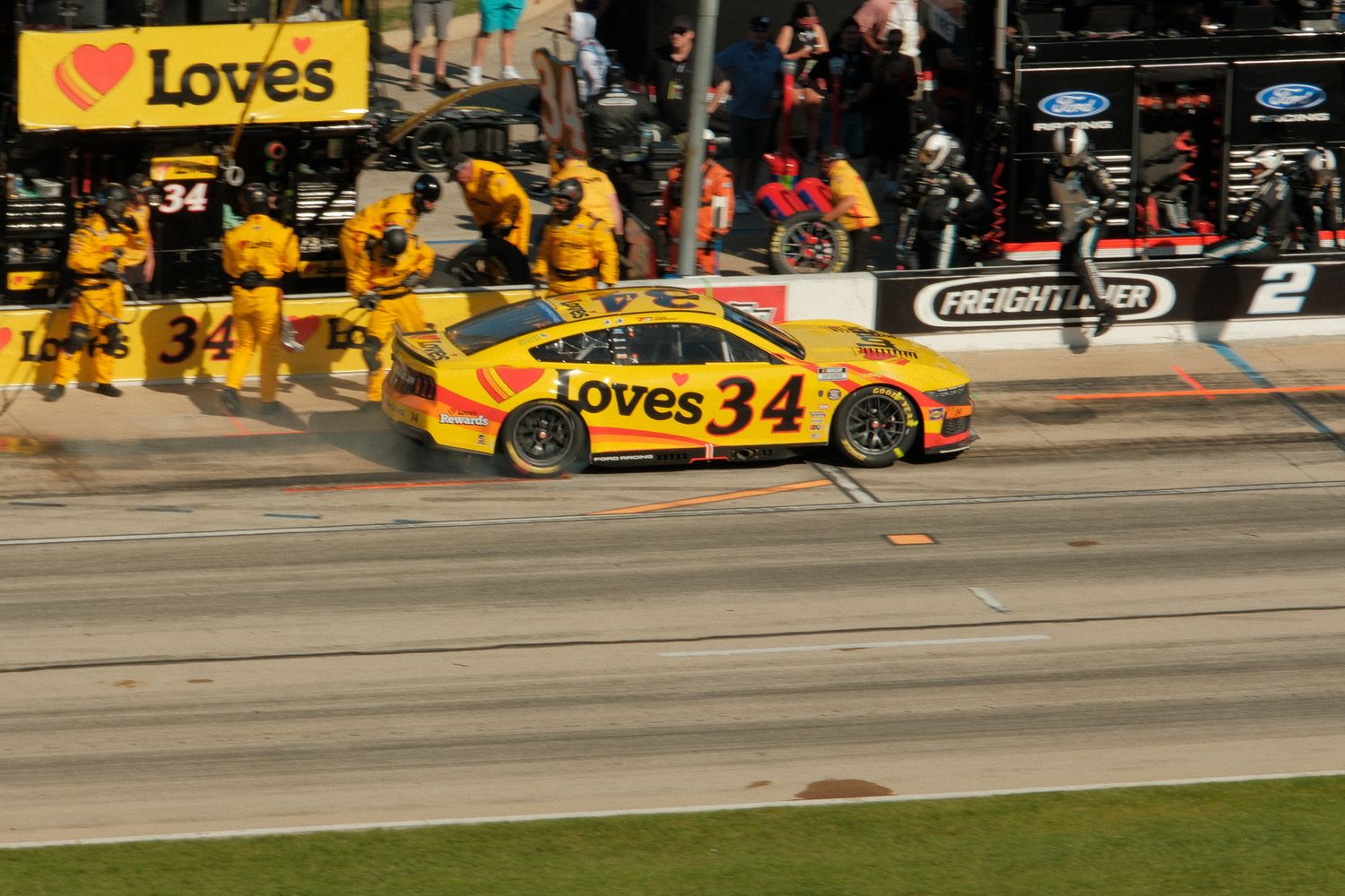 Loves Travel Stops number 34 NASCAR Ford makes a pit stop with crew members in yellow uniforms.