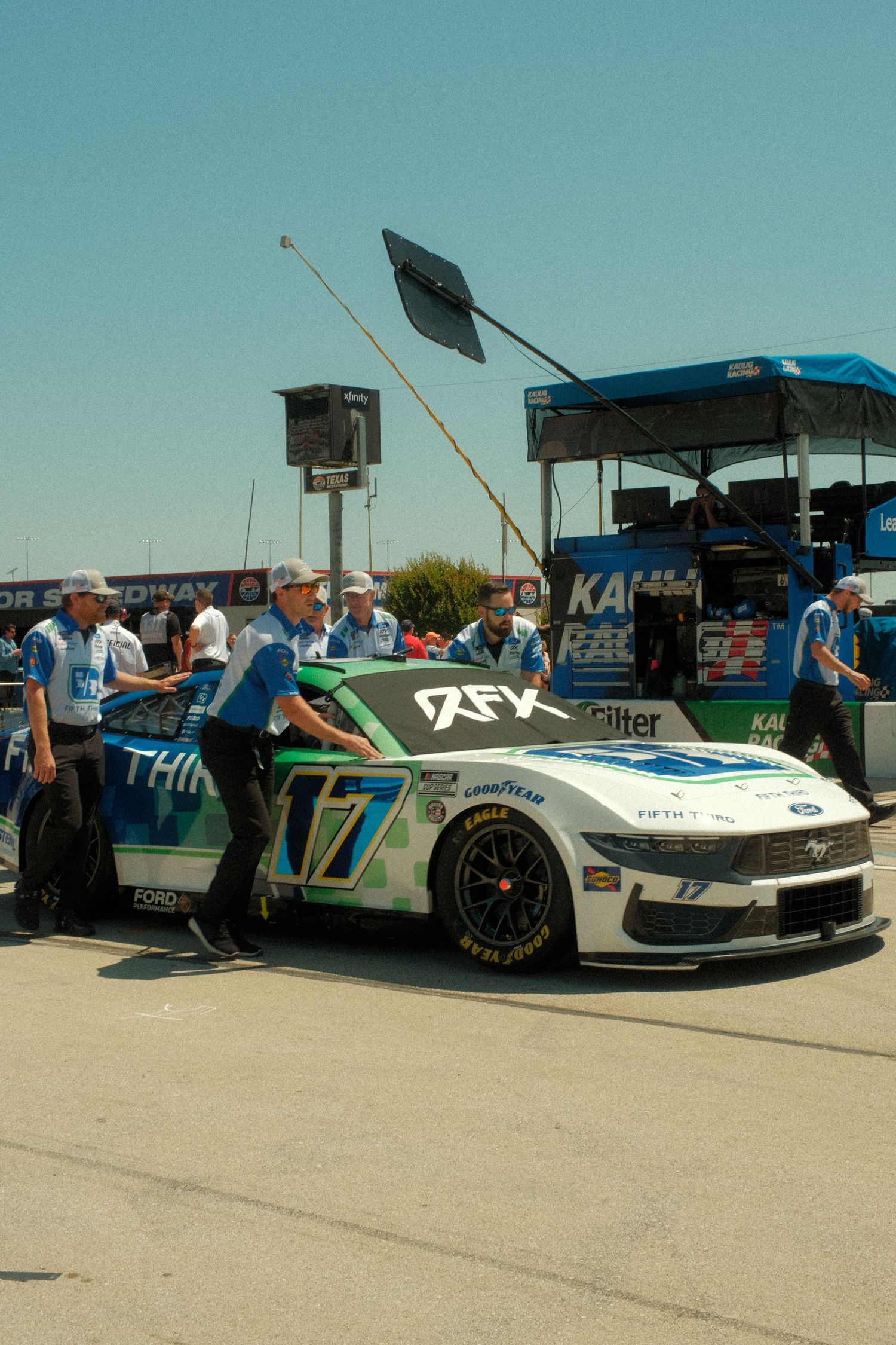 NASCAR pit crew members push the RFK Racing number 17 Ford Mustang race car through the garage area.