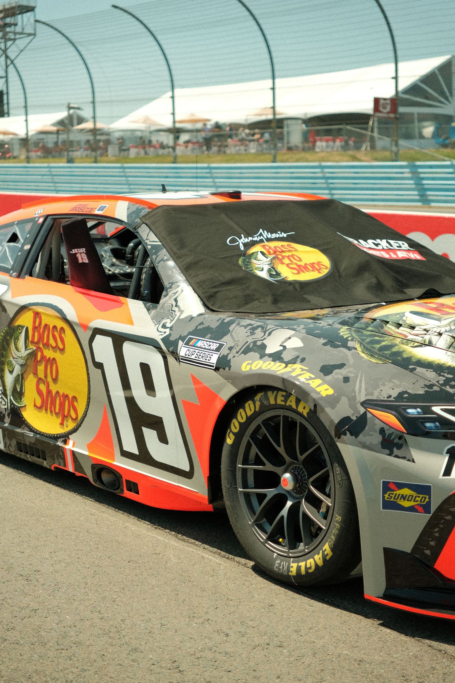 Bass Pro Shops sponsored NASCAR number 19 race car on pit road at a sunny racing circuit.