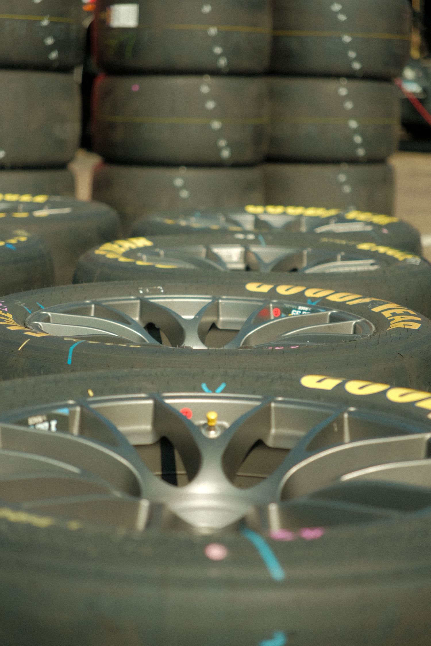 Rows of Goodyear Eagle NASCAR racing tires stacked on rims in a pit area.