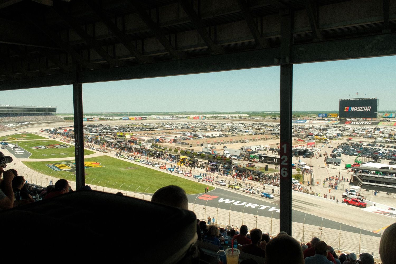 Aerial view of a NASCAR race track with packed grandstands, pit road, and infield visible on a sunny day.