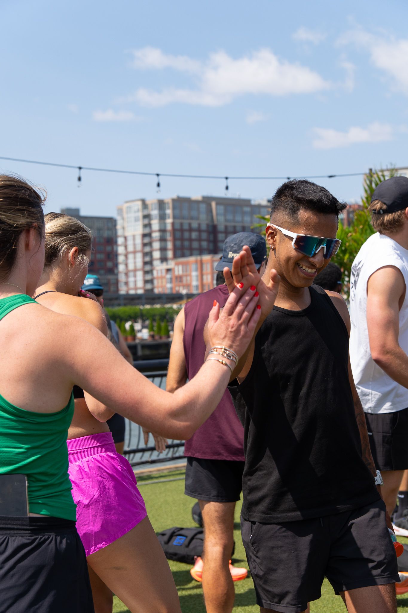 Two athletes high-fiving outdoors on a rooftop turf field on a sunny day, wearing athletic wear and sunglasses.