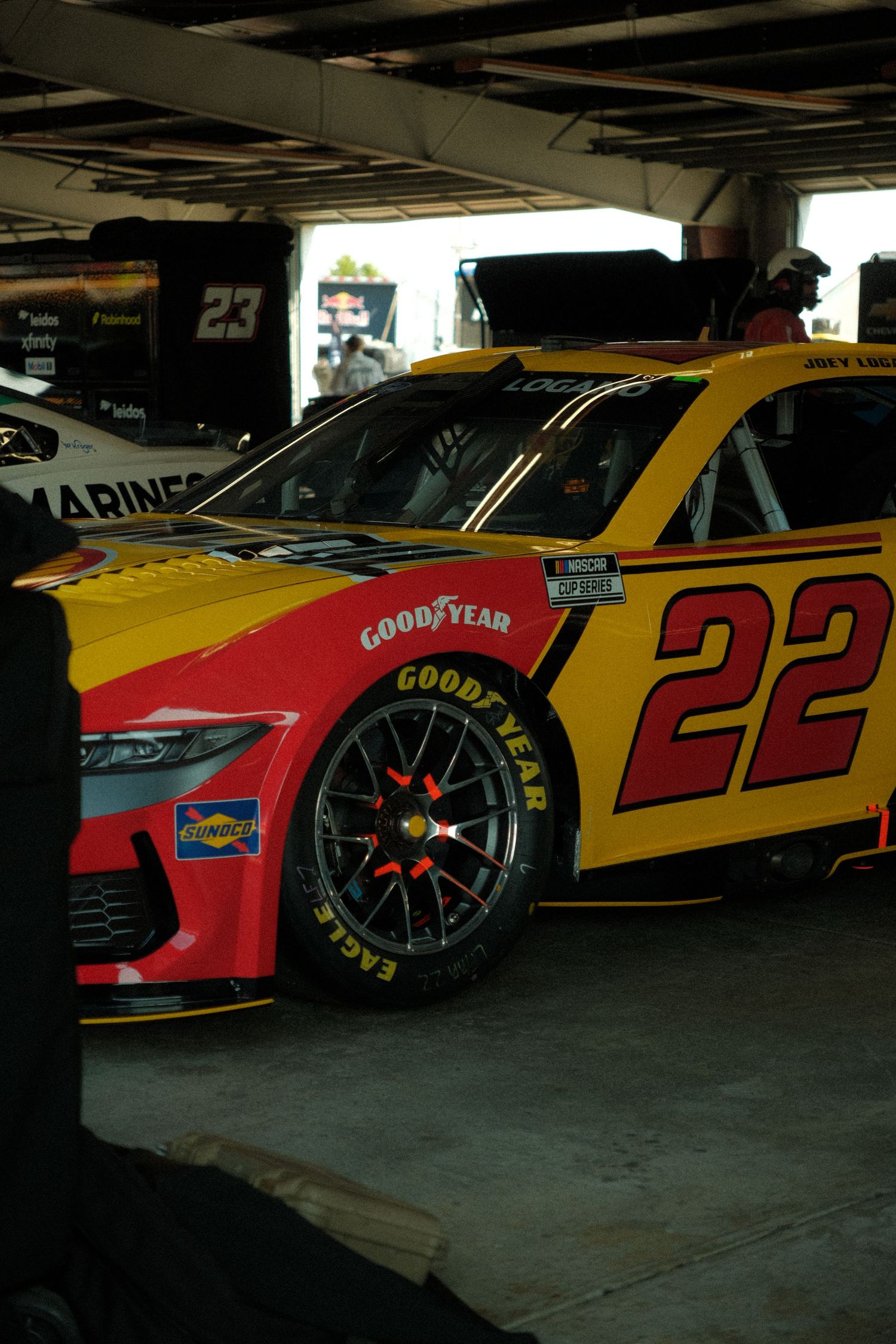 NASCAR #22 Joey Logano red and yellow Ford Mustang race car with Goodyear Eagle tires in the garage area.