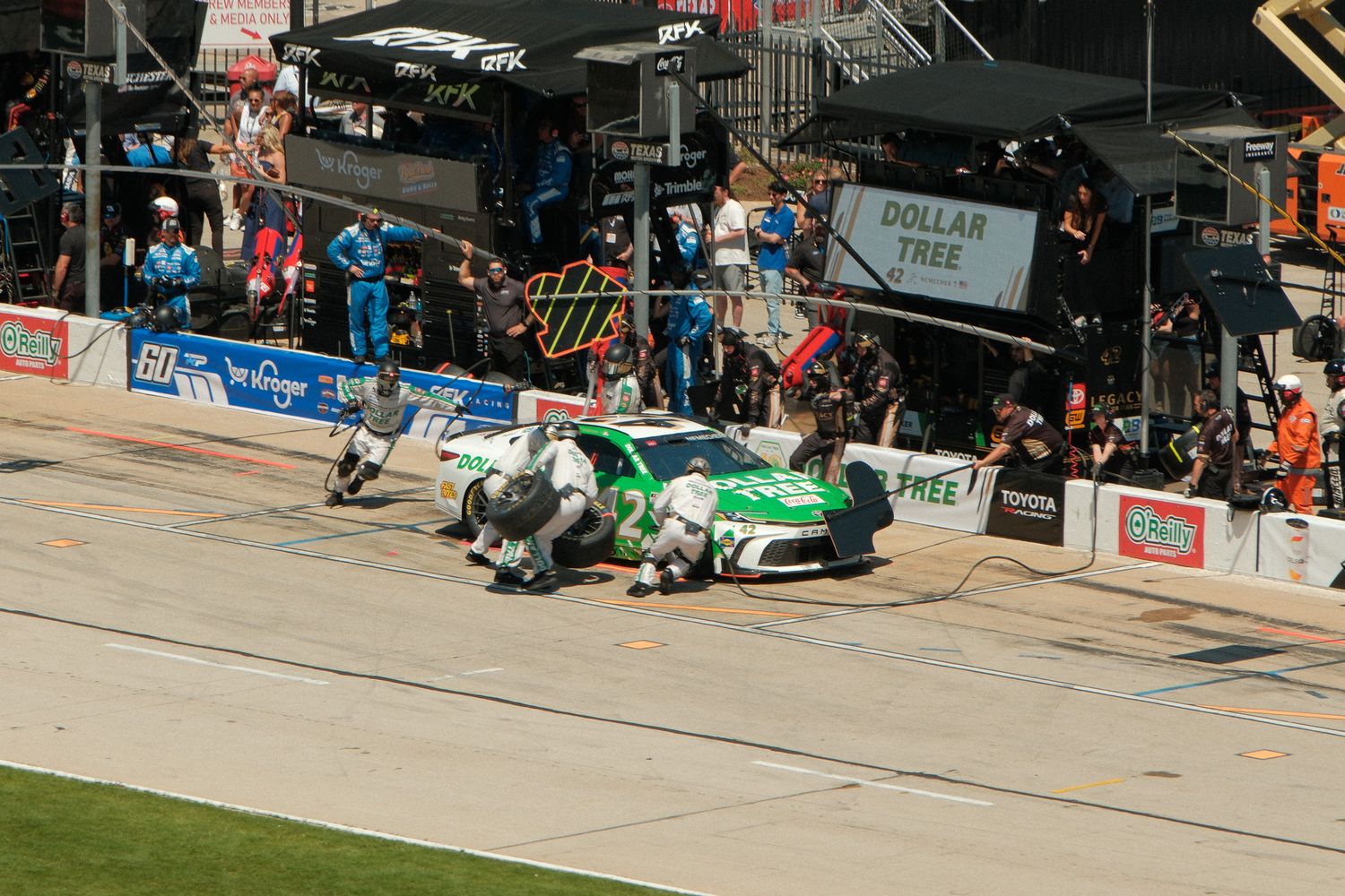NASCAR pit crew services a green and white race car during a pit stop at a busy speedway race event.