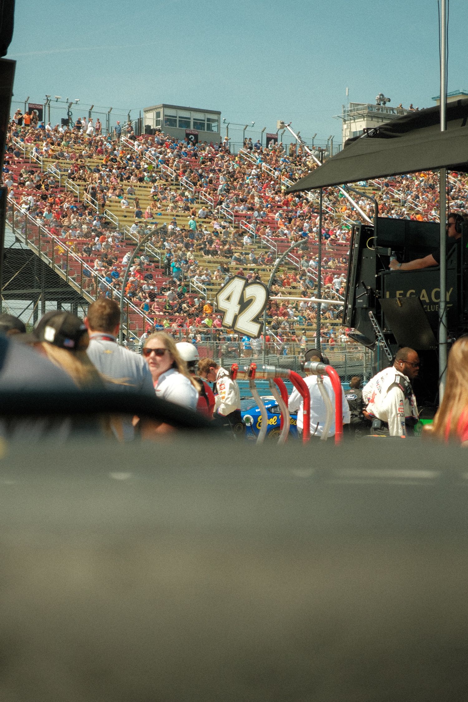 A packed grandstand of fans watches NASCAR Cup Series race action near the number 42 John Hunter Nemechek pit box at Watkins Glen.