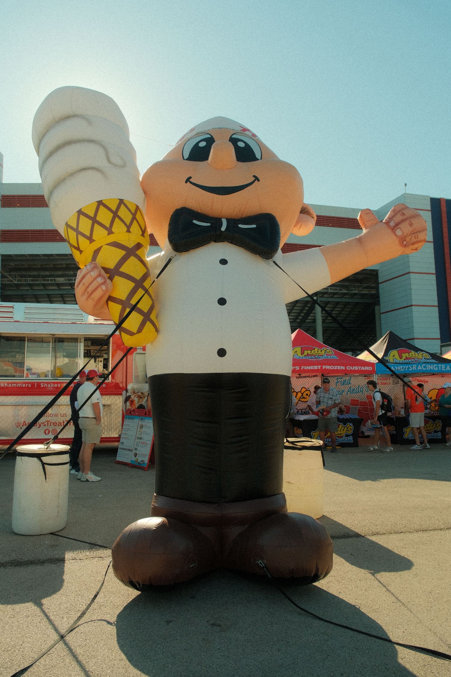 Large inflatable waiter mascot holding an ice cream cone at an outdoor food festival on a sunny day.
