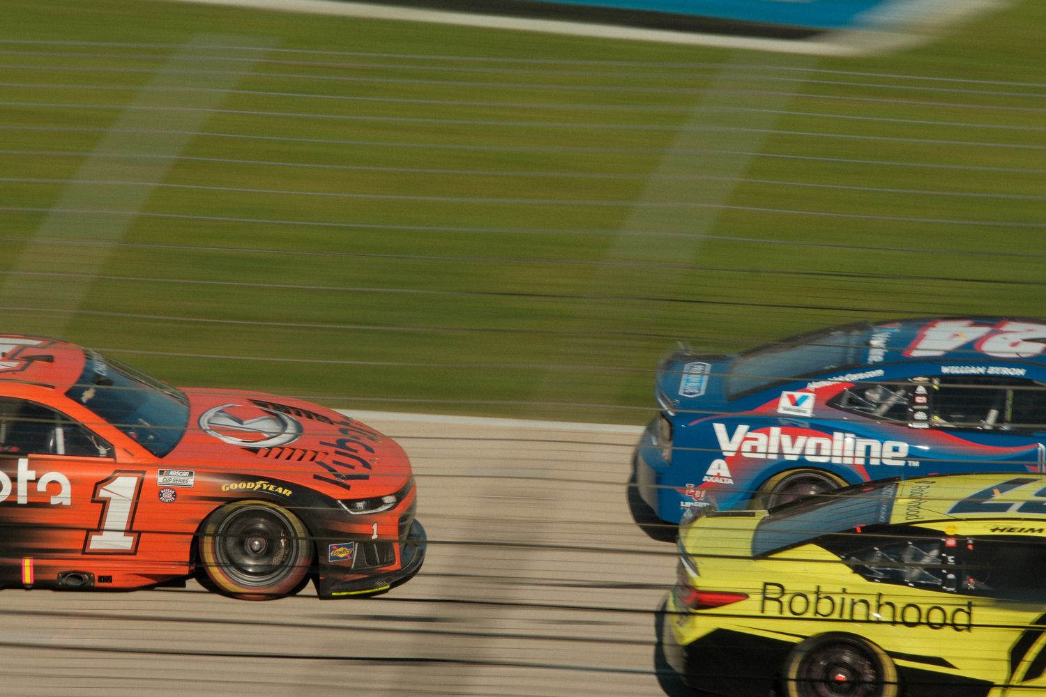 Three NASCAR stock cars race side by side on a track, featuring Roto, Valvoline, and Robinhood sponsors.