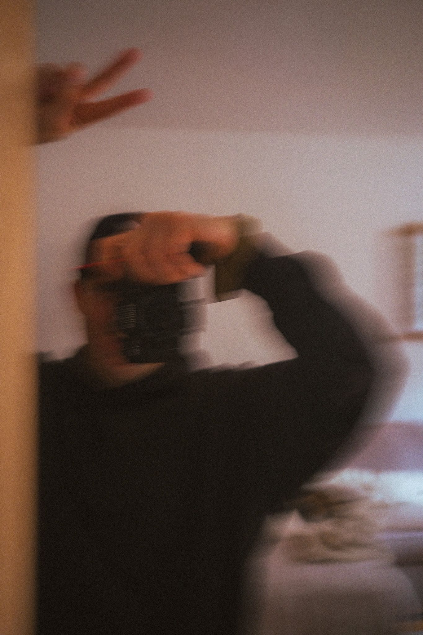 Blurry motion shot of a person taking a mirror selfie with a camera indoors.