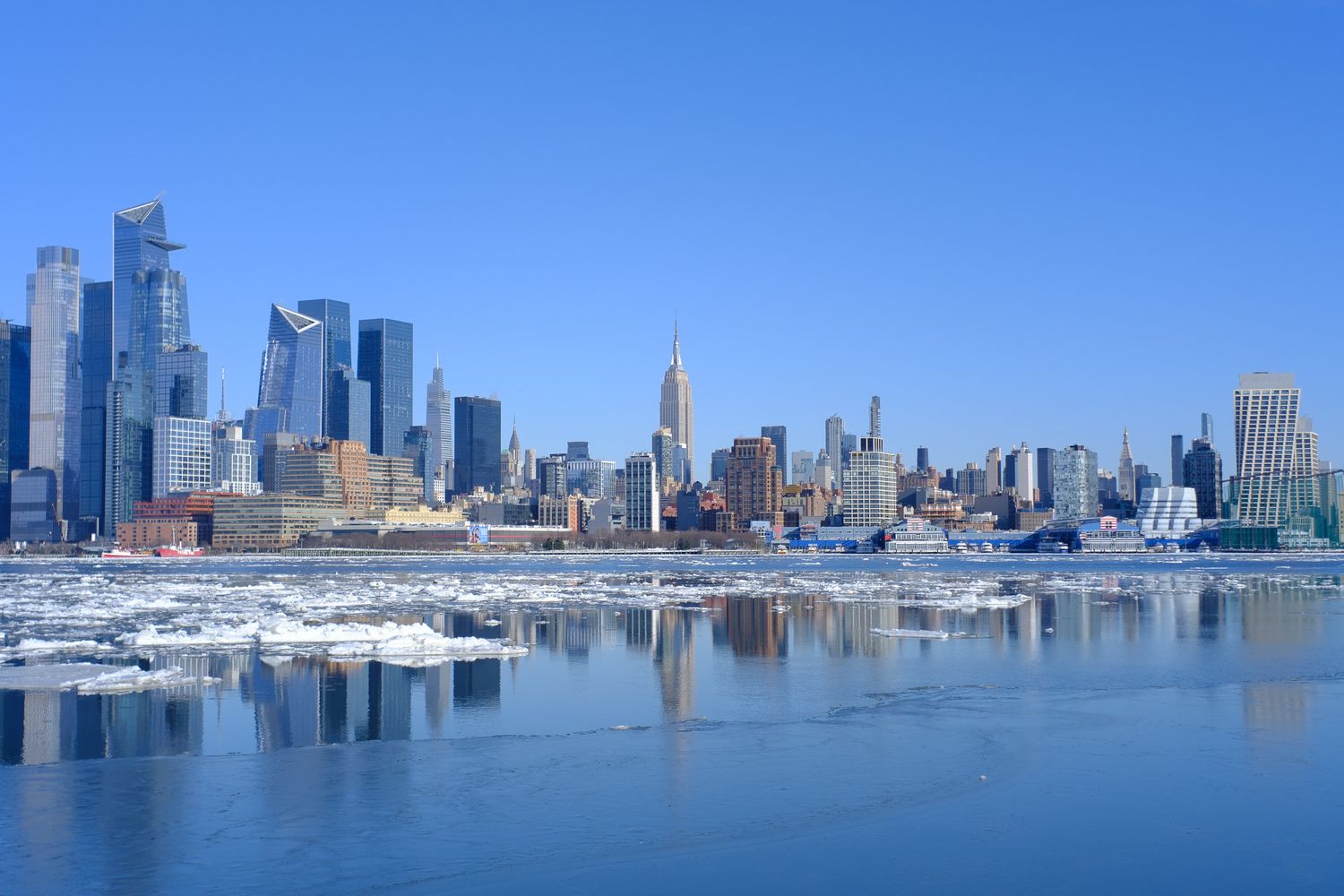 New York City skyline with Empire State Building across icy Hudson River on clear winter day from Hoboken, NJ.