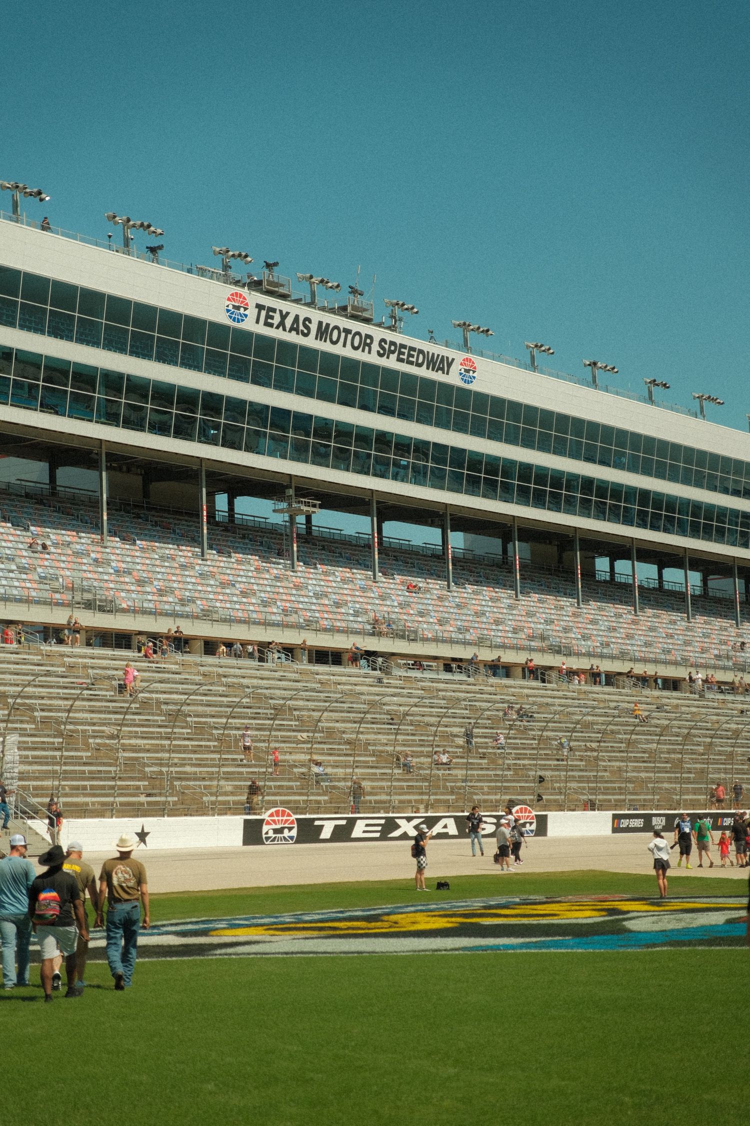 Texas Motor Speedway grandstands with fans on race day under clear blue skies, featuring the iconic speedway signage.