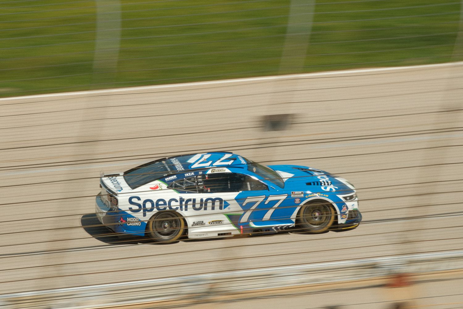 NASCAR race car #77 with Spectrum sponsorship speeding on track.