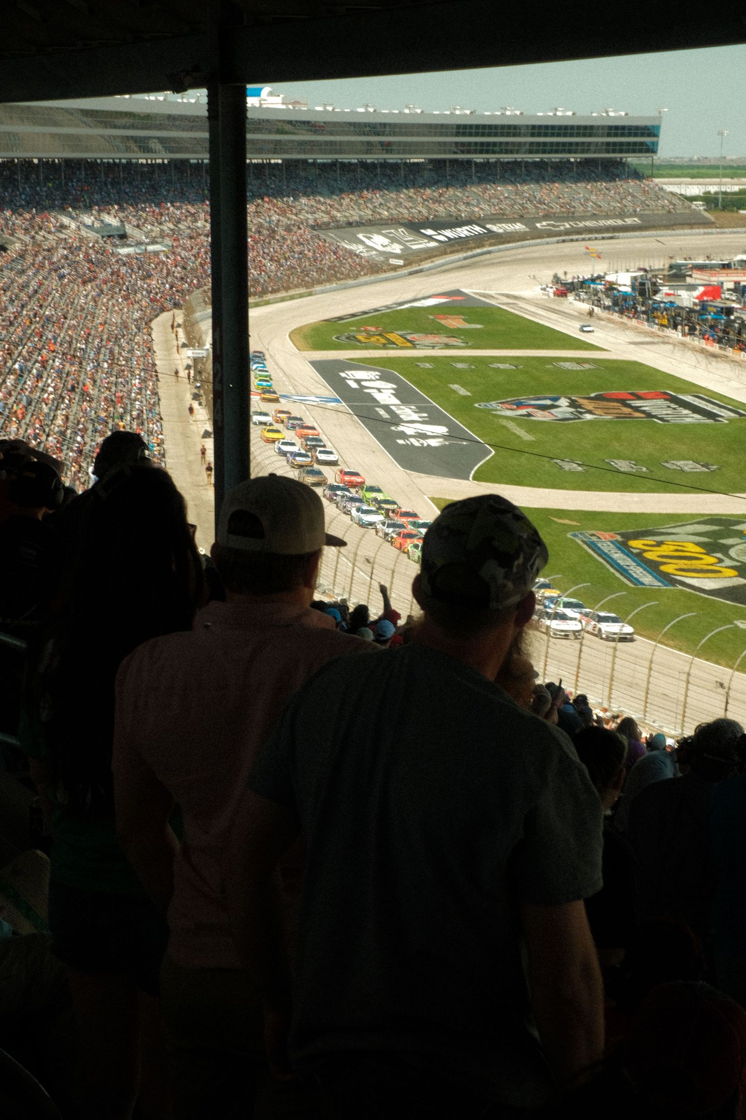 Aerial view of packed NASCAR race stadium with spectators watching colorful race cars on track below.