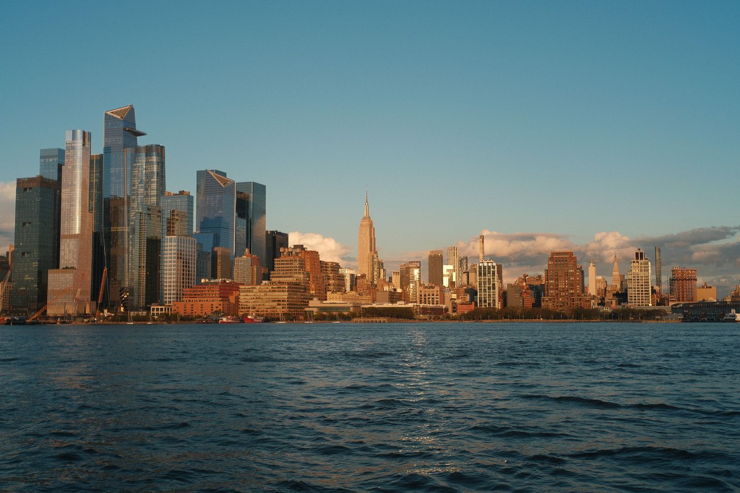 The Manhattan skyline glows golden at sunset with the Empire State Building visible across the water from Hoboken, NJ.