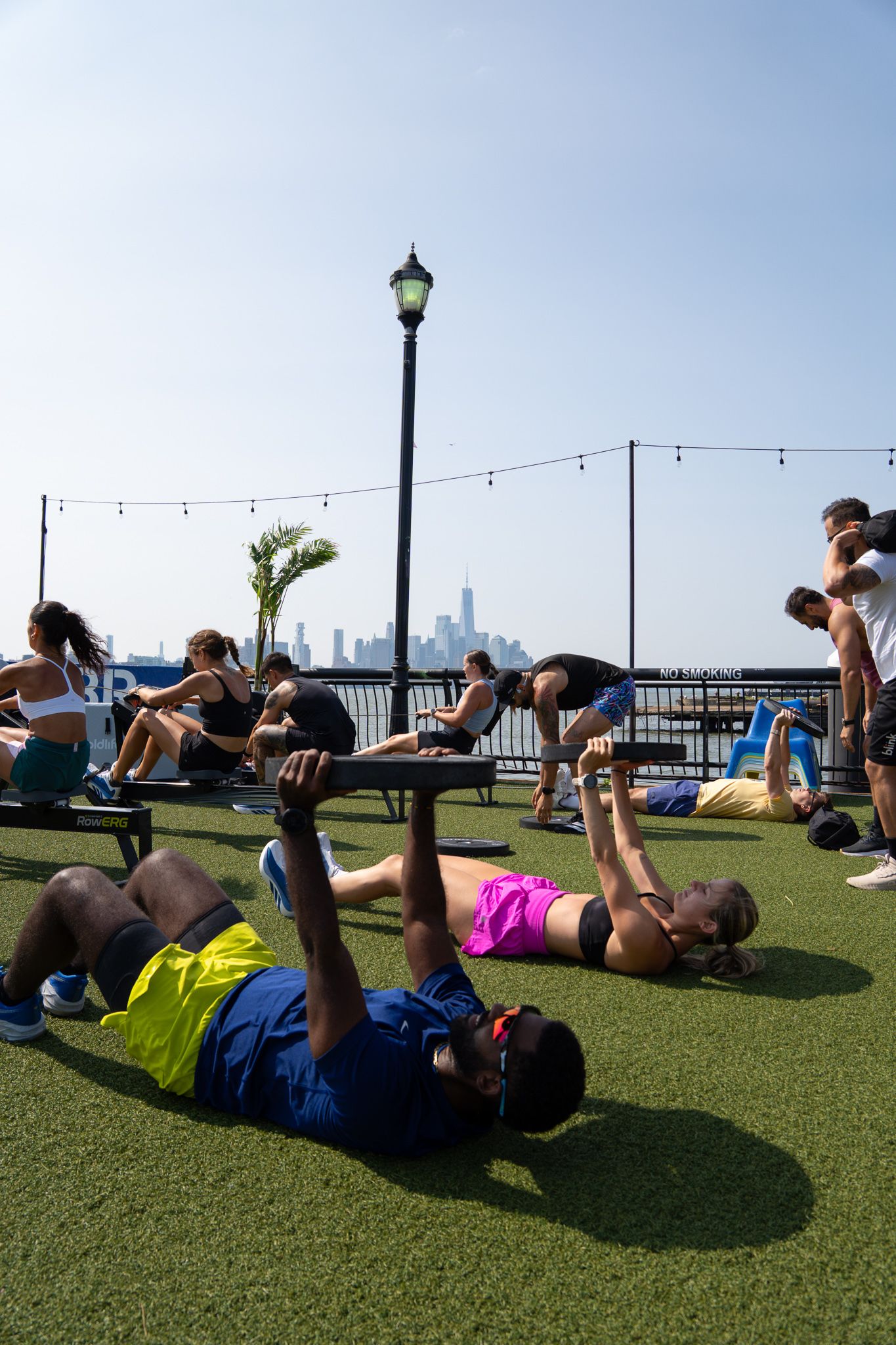 Group of people exercising outdoors on grass with NYC skyline visible in the background on a sunny day.