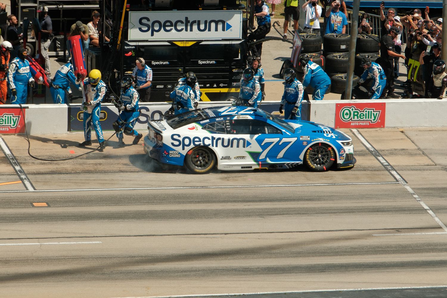 NASCAR No. 77 Spectrum-sponsored race car makes a pit stop with crew members in blue uniforms at a speedway.