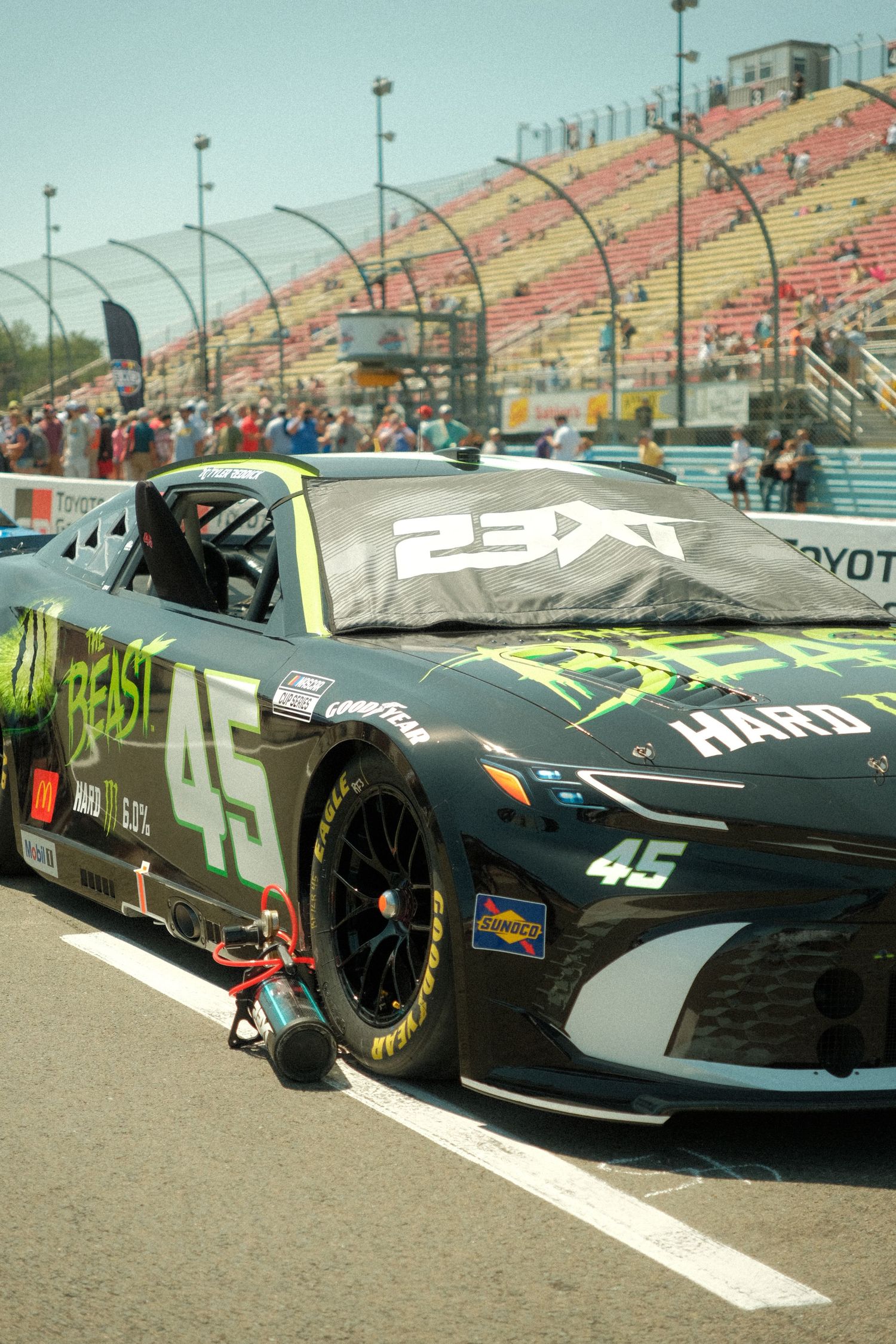 NASCAR 23XI Racing #45 Beast Hard Line sponsored black car on pit road at sunny race track.