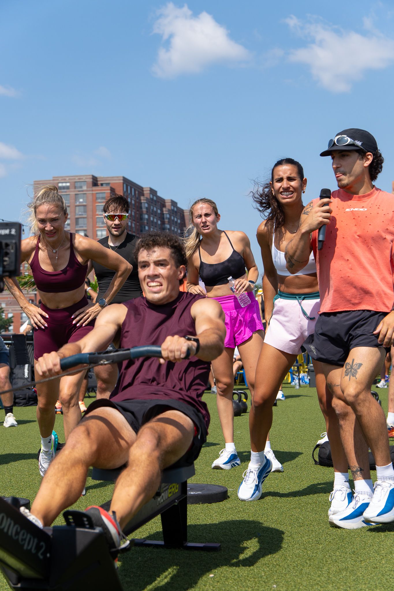 Group of fit athletes cheering during an outdoor rowing machine workout on a rooftop gym.