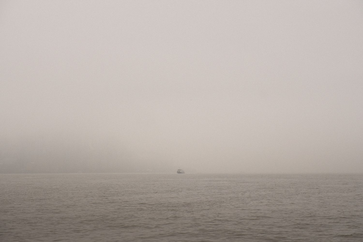 A small NY Waterway boat sits alone on the calm gray misty Hudson River under an overcast sky.