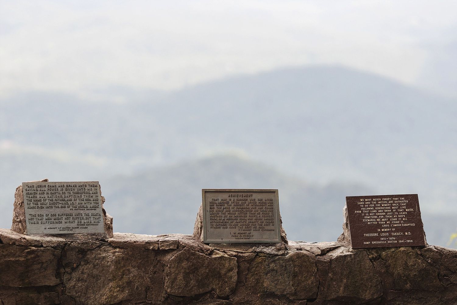Three stone markers sit atop a rustic wall with misty mountains in the background.
