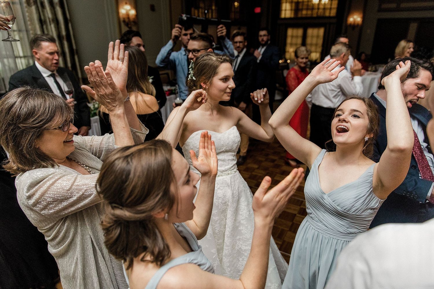 Wedding guests dancing and celebrating with raised arms on the dance floor.
