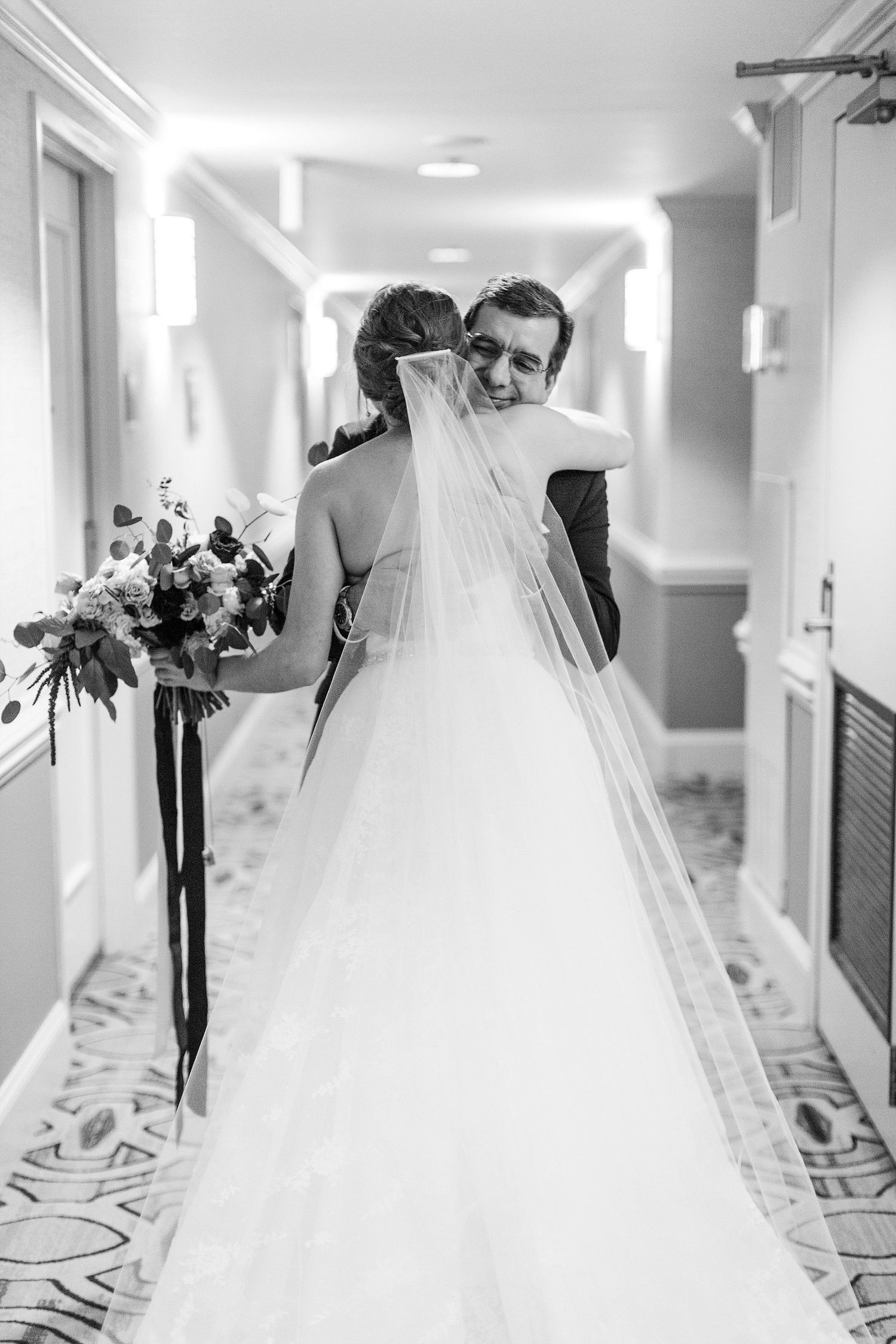 A black and white wedding photo capturing a tender moment in a bright hallway.
