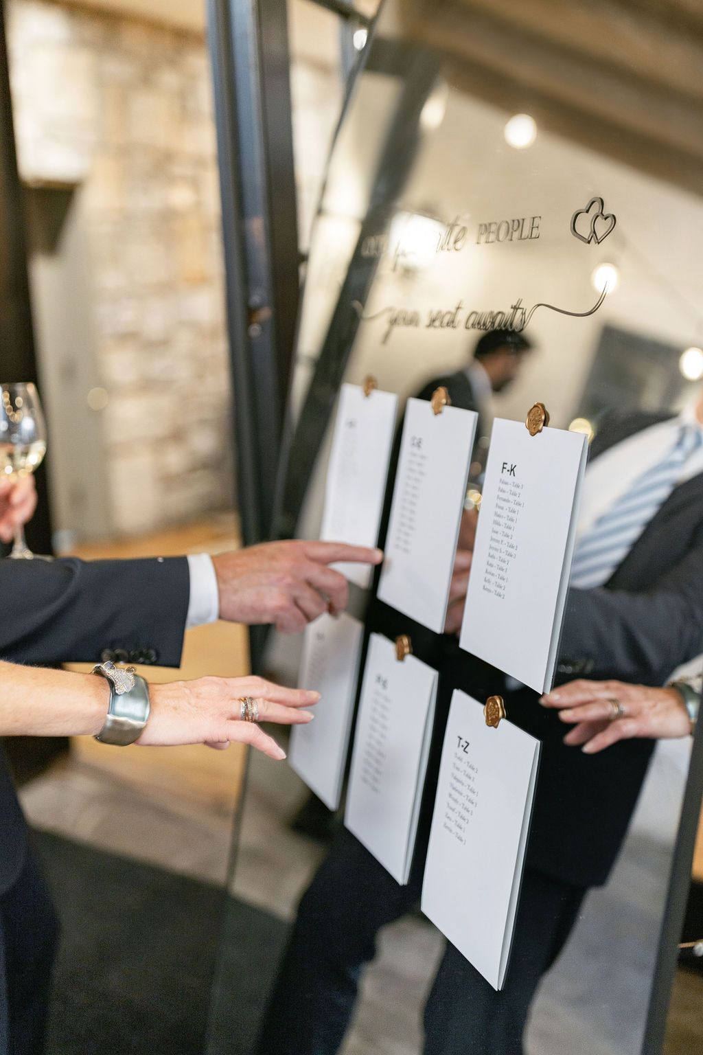 Wedding seating chart display with multiple paper lists clipped to a board being reviewed by guests.