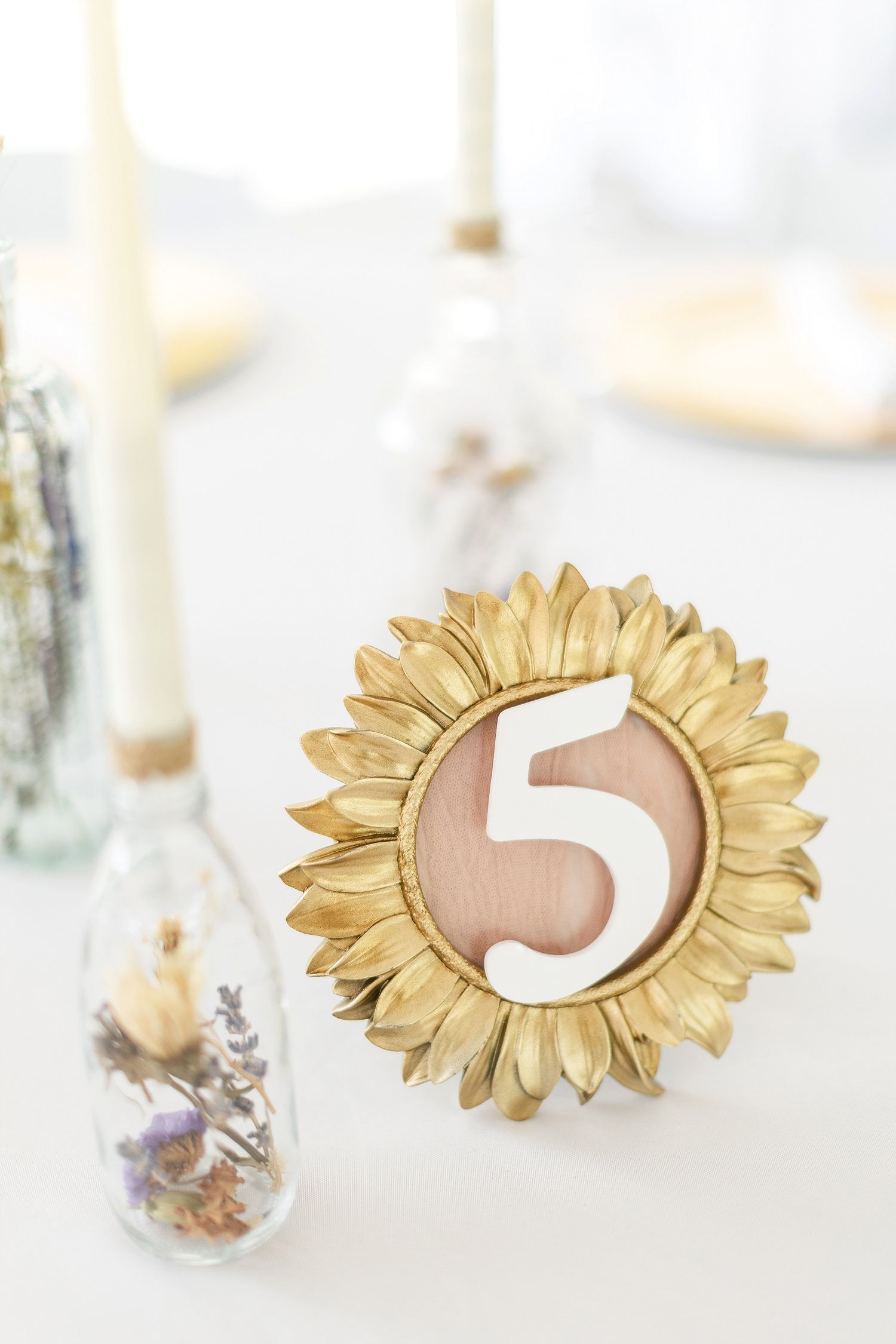 Gold sunflower-shaped table number holder displaying number 5 on white tablecloth.