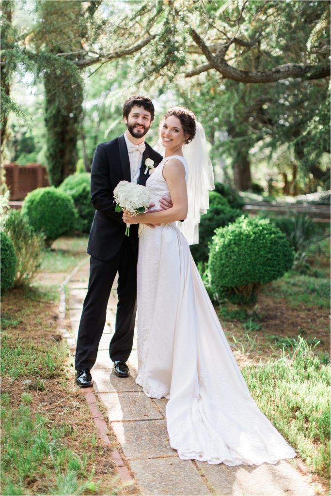 Elegant wedding portrait of couple on garden path with lush greenery background.