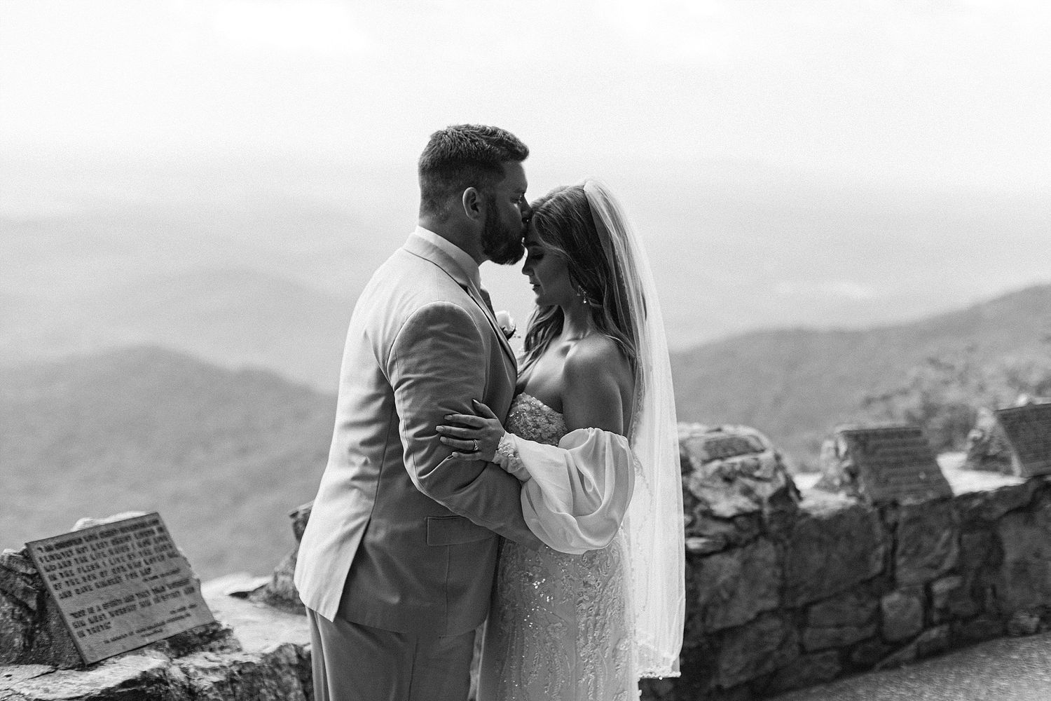 A tender black and white wedding portrait captured against a mountainous backdrop.